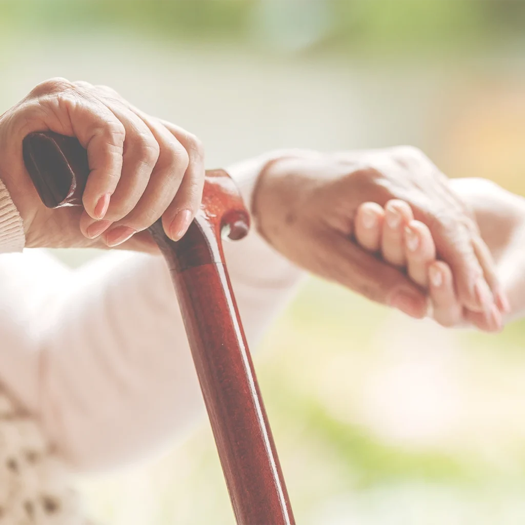 Ältere Person hält einen Gehstock, während eine helfende Hand Unterstützung anbietet