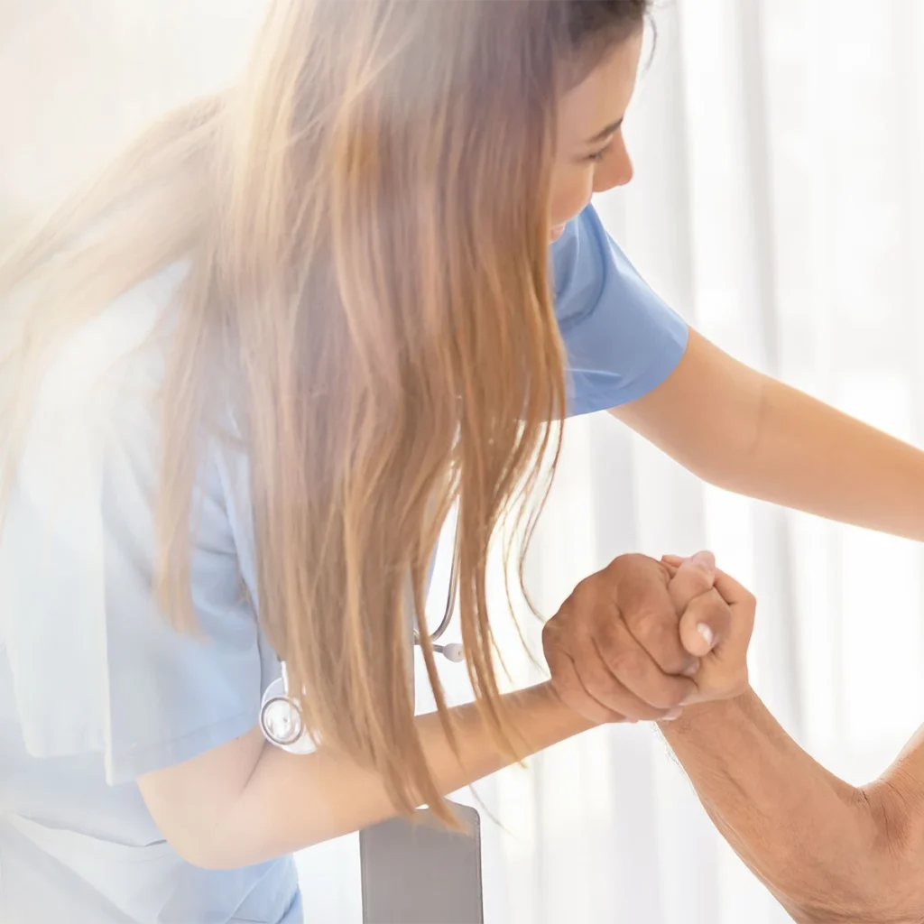 Pflegerin unterstützt eine ältere Person beim Aufstehen und hält ihre Hand zur Hilfe